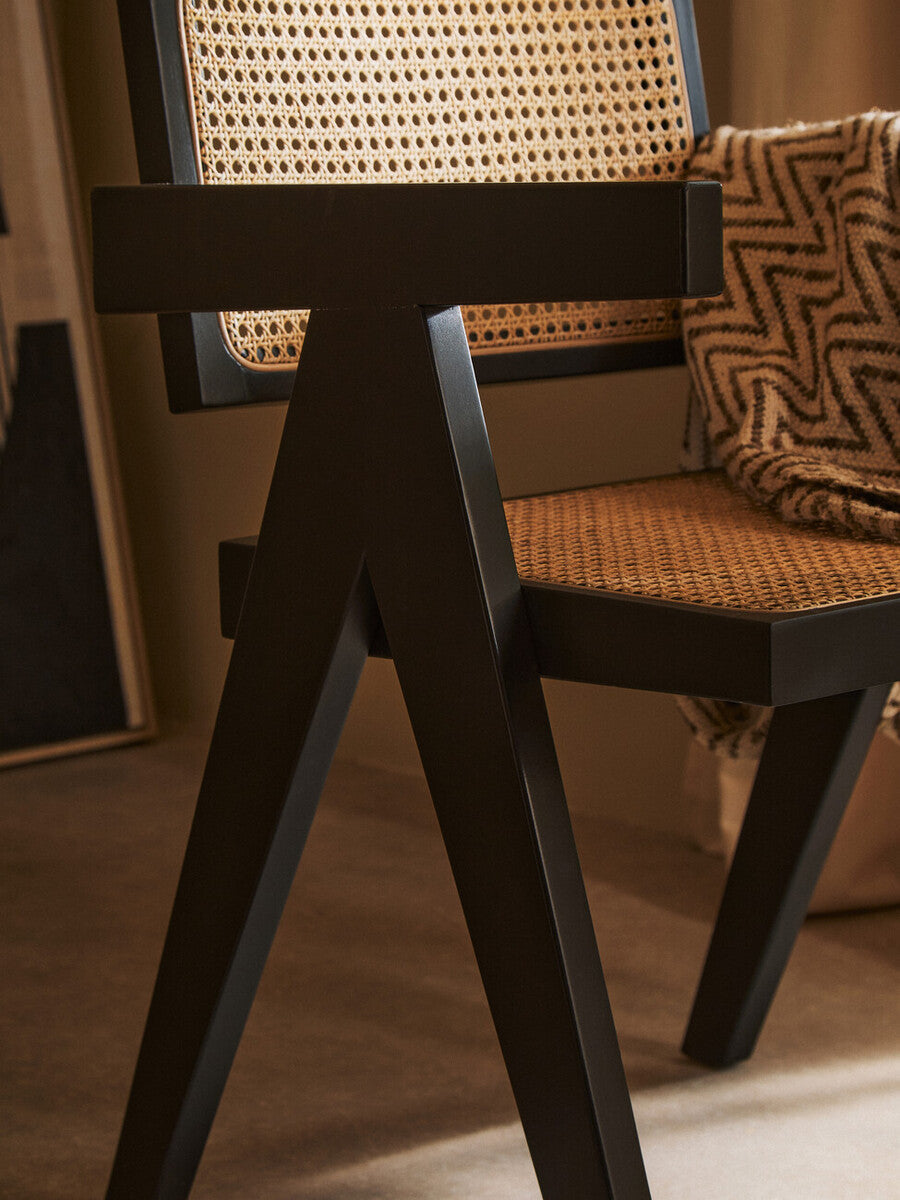 Close-up of a black wooden chair with woven seat and backrest in a room setting.