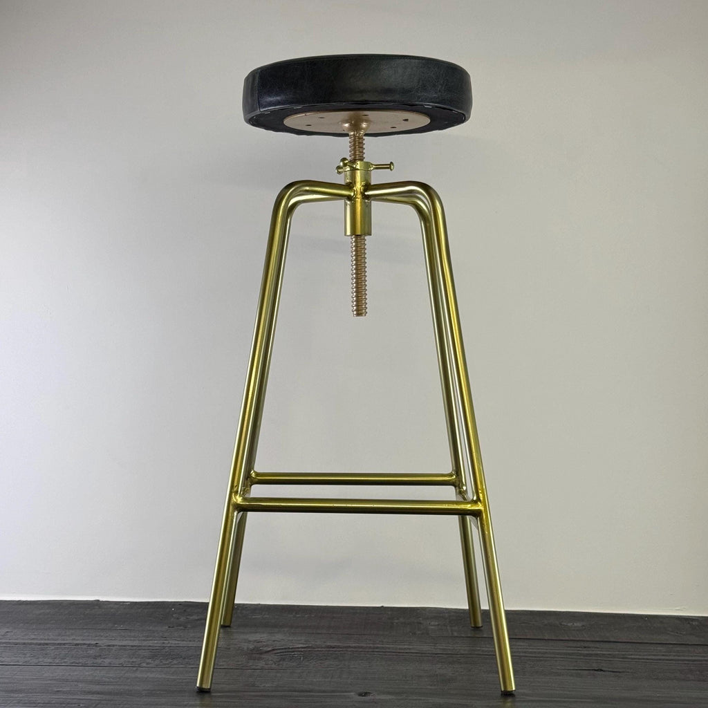 Bar stool with gold metal legs and black seat on a plain background