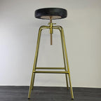 Bar stool with gold metal legs and black seat on a plain background