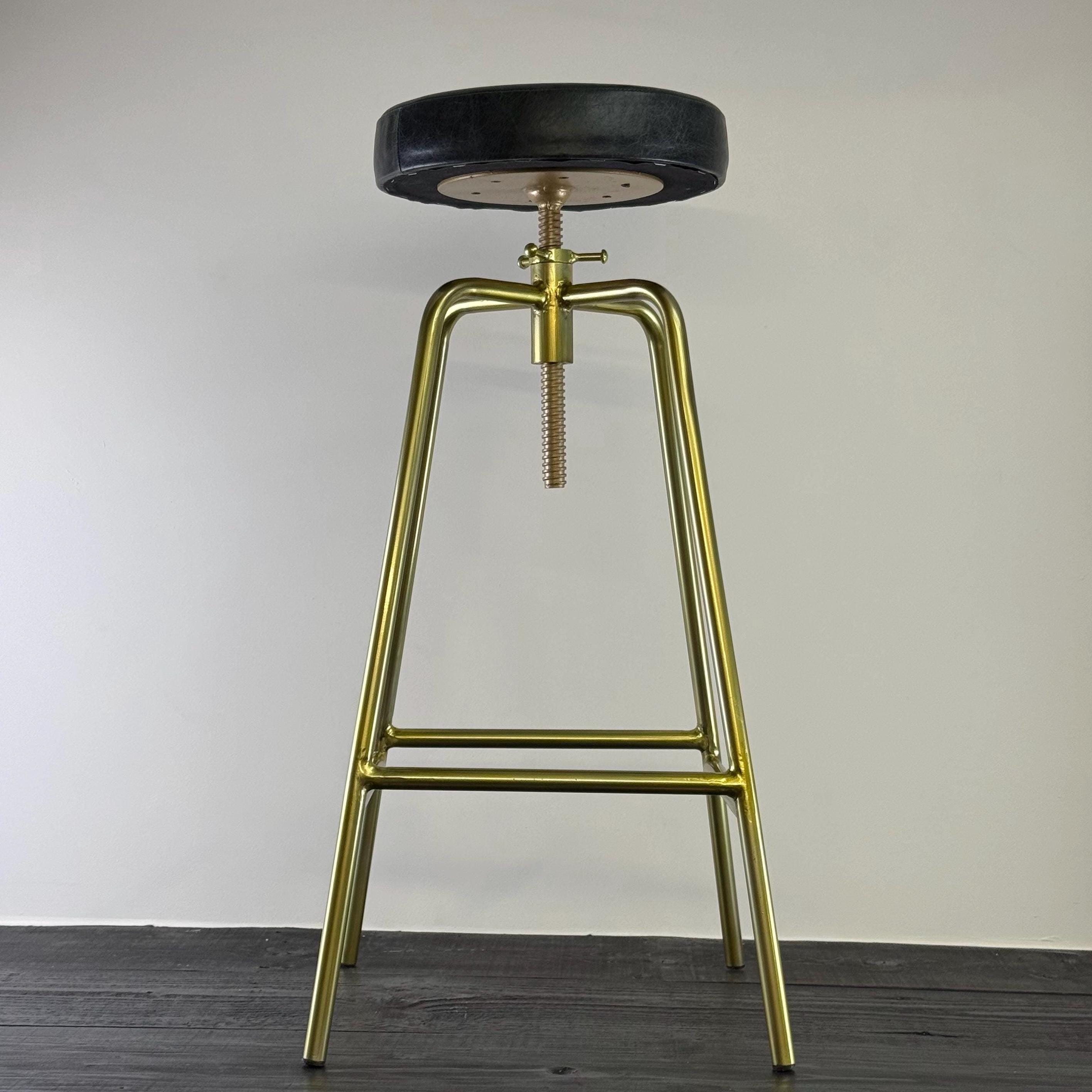 Bar stool with gold metal legs and black seat on a plain background