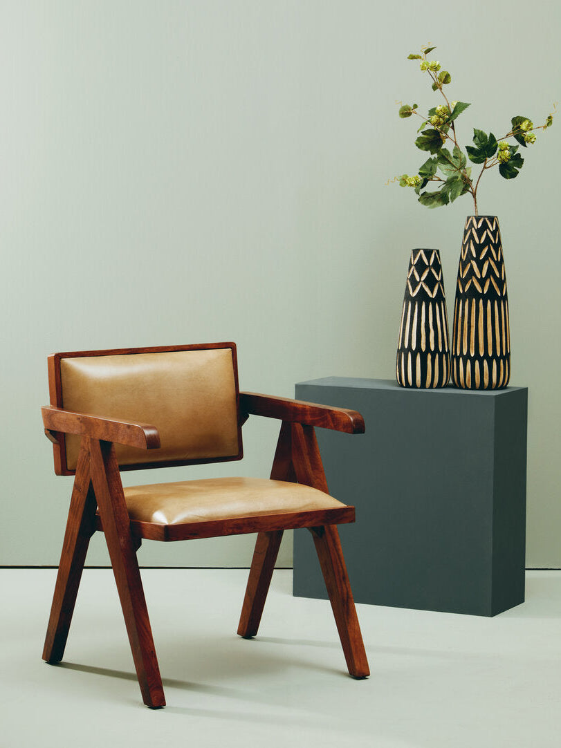 Brown wooden leather chair next to vases on light green backdrop