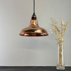 Copper pendant light hanging above a clear vase with dried plants on a gray background