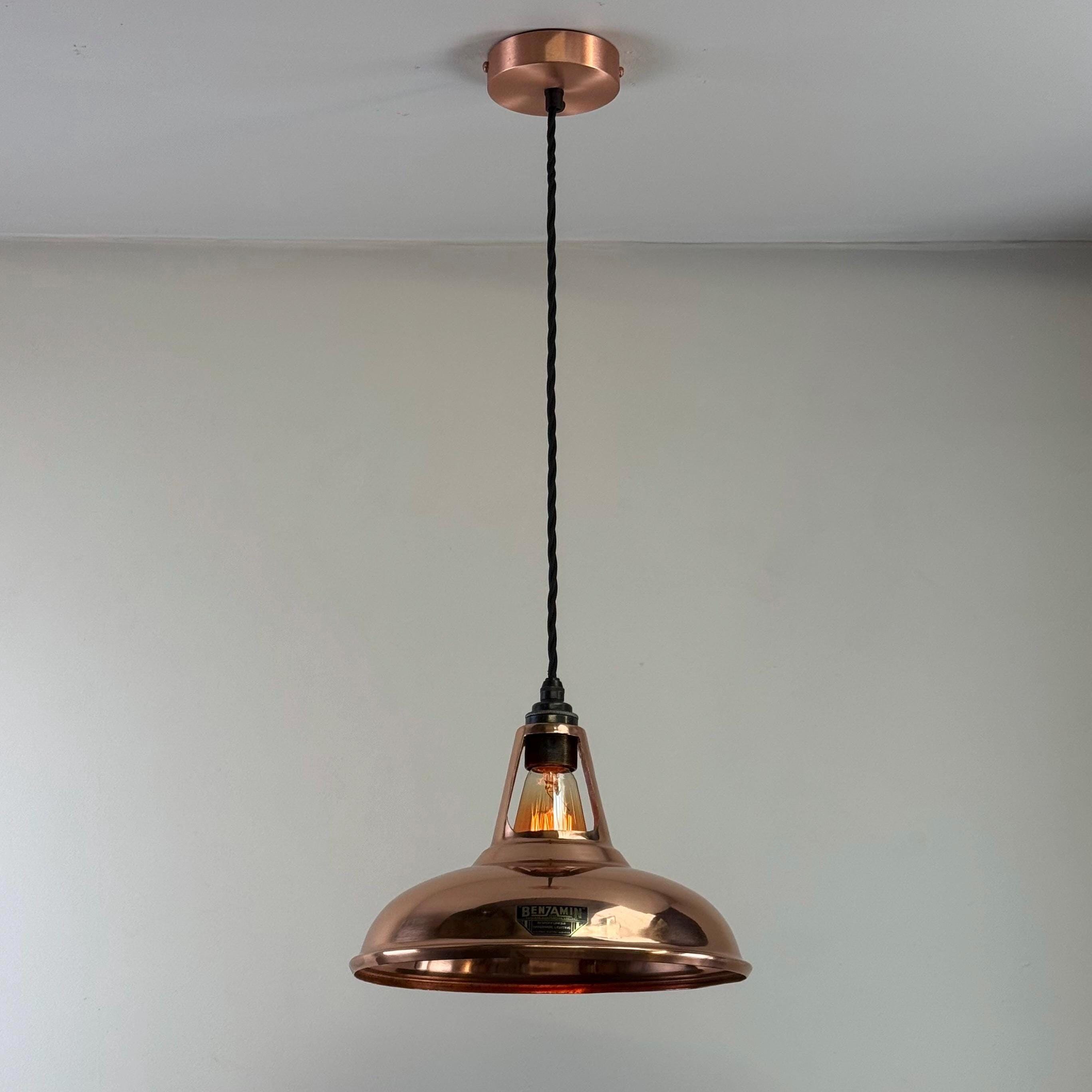 Copper pendant light hanging from a ceiling against a plain background