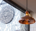 Copper pendant light hanging in front of a decorative window