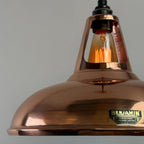 Copper pendant light with a visible brand label on a gray background