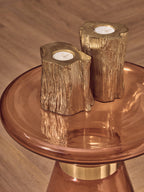 Two gold candle holders shaped like tree stumps on a orange glass side table