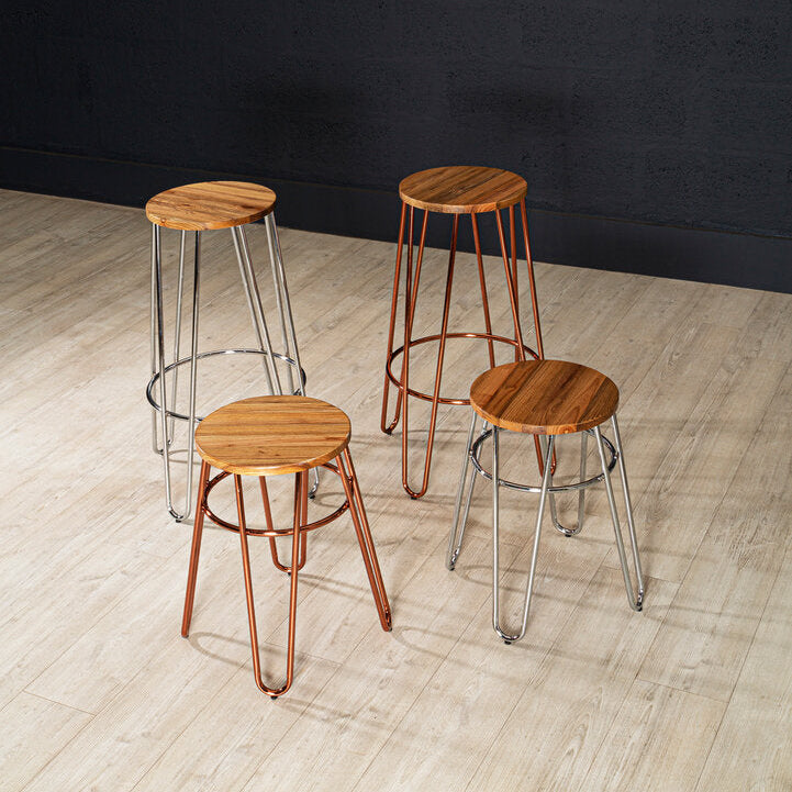 Four bar stools with wooden seats and metal legs on a wooden floor against a black wall.