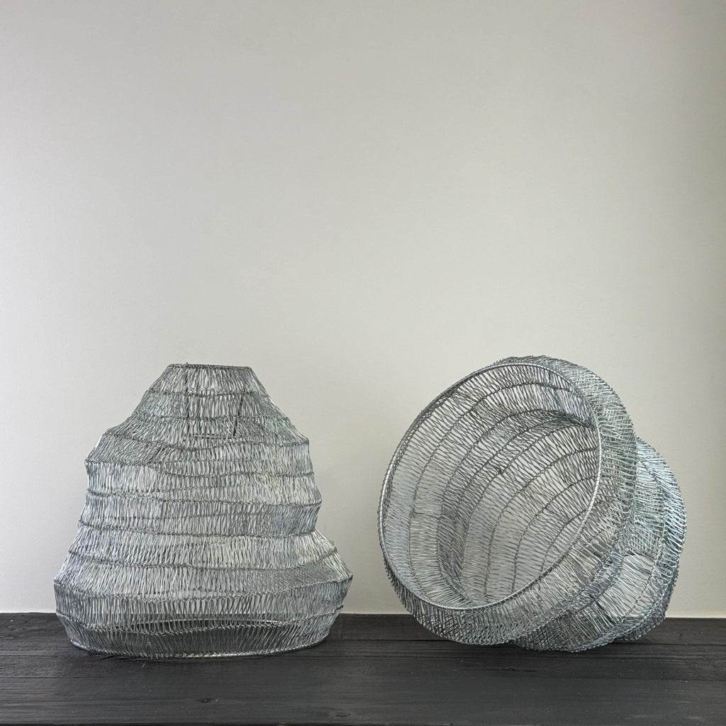 Two wire mesh lamp shades on a dark surface with a plain background