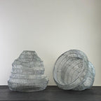 Two wire mesh lamp shades on a dark surface with a plain background