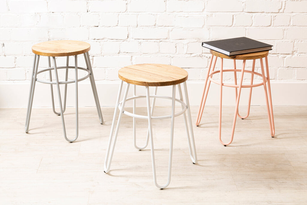 Three stools with different designs and colors against a white brick wall.