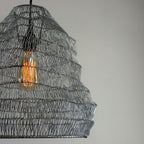 Woven pendant light with a visible bulb against a neutral background