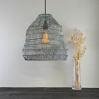Textured pendant light fixture hanging above a wooden surface with a vase of dried flowers.
